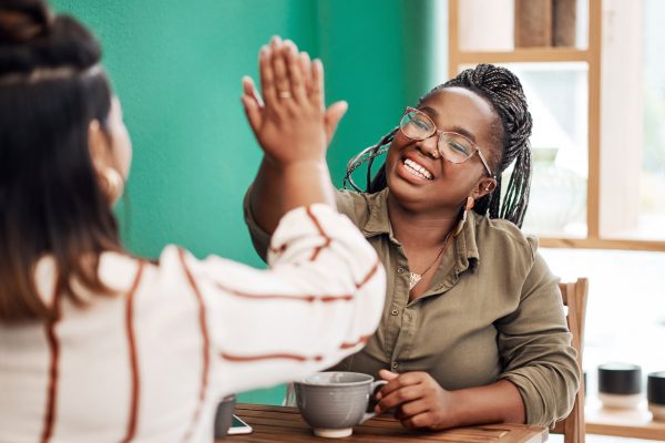 Shot of two young women giving each other a high five in a cafe